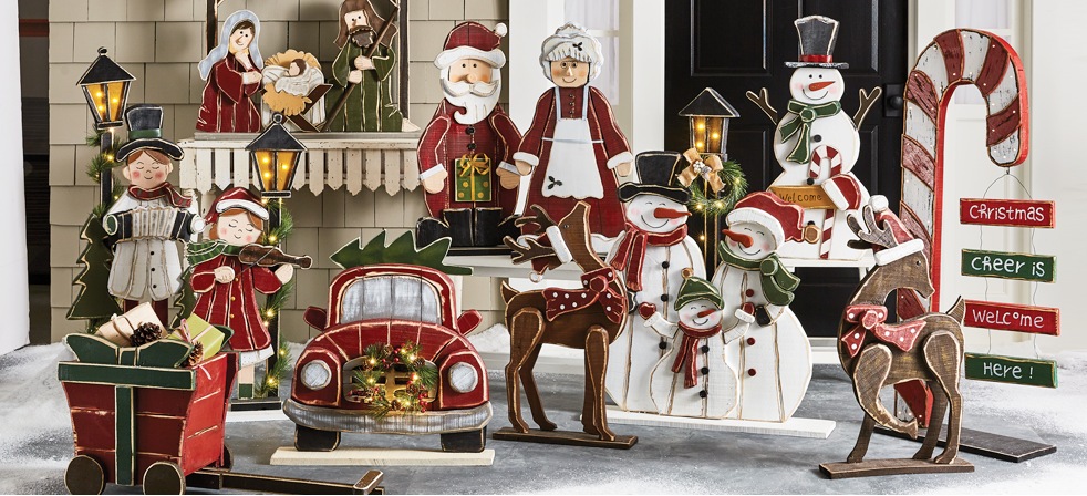 Shop Now Banner Image: Collection of Chunky Wood Cutouts for winter including reindeer, carolers, nativity scene, Mr. and Mrs. Claus, and more pictured on front porch.