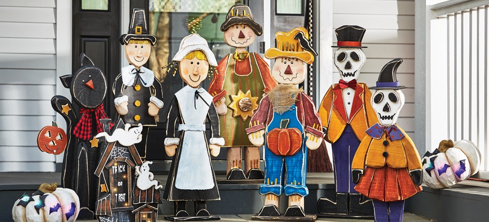 Shop Now Banner Image: Collection of Chunky Wood Cutouts for fall including scarecrows, skeletons, black cat, haunted house and pilgrims, pictured on front porch stairs.